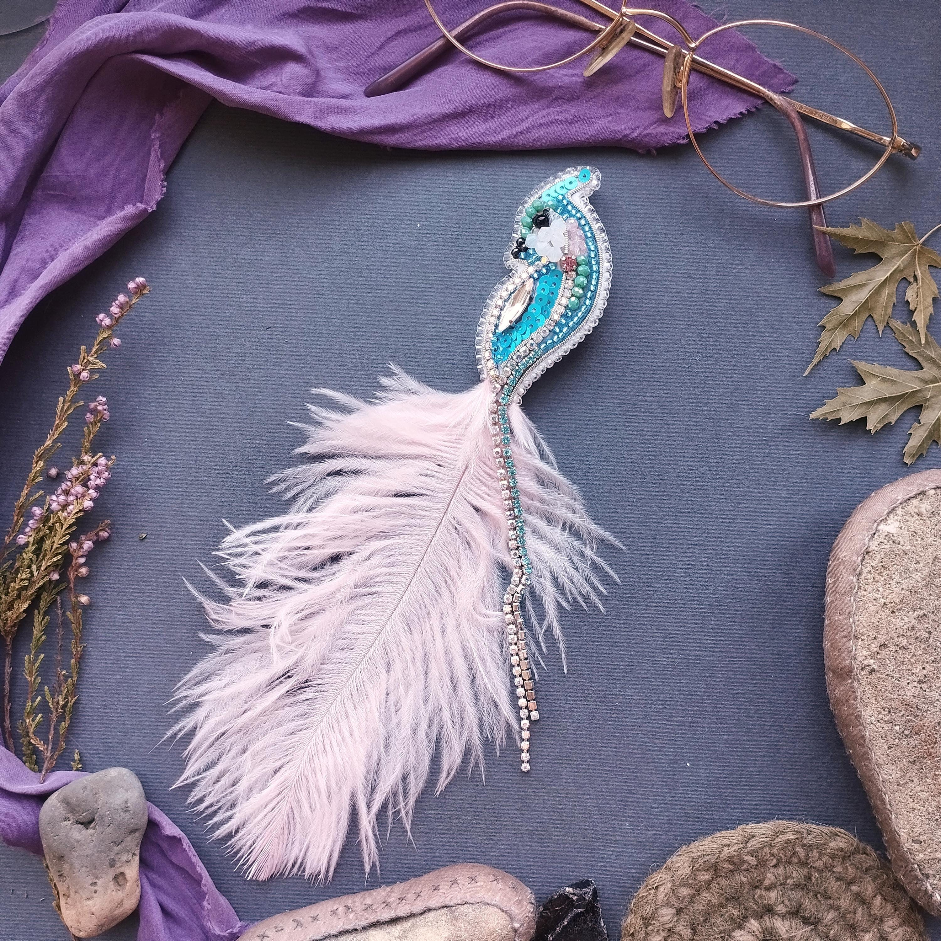 a close-up view of a feather with a beaded design, surrounded by various objects such as a pair of glasses, a purple cloth, and some rocks.
